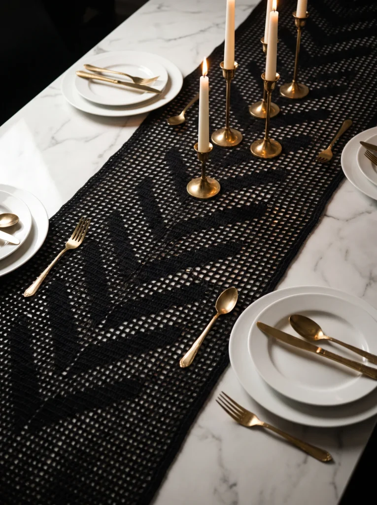 black filet crochet table runner on a marble table with gold candlesticks and white plates